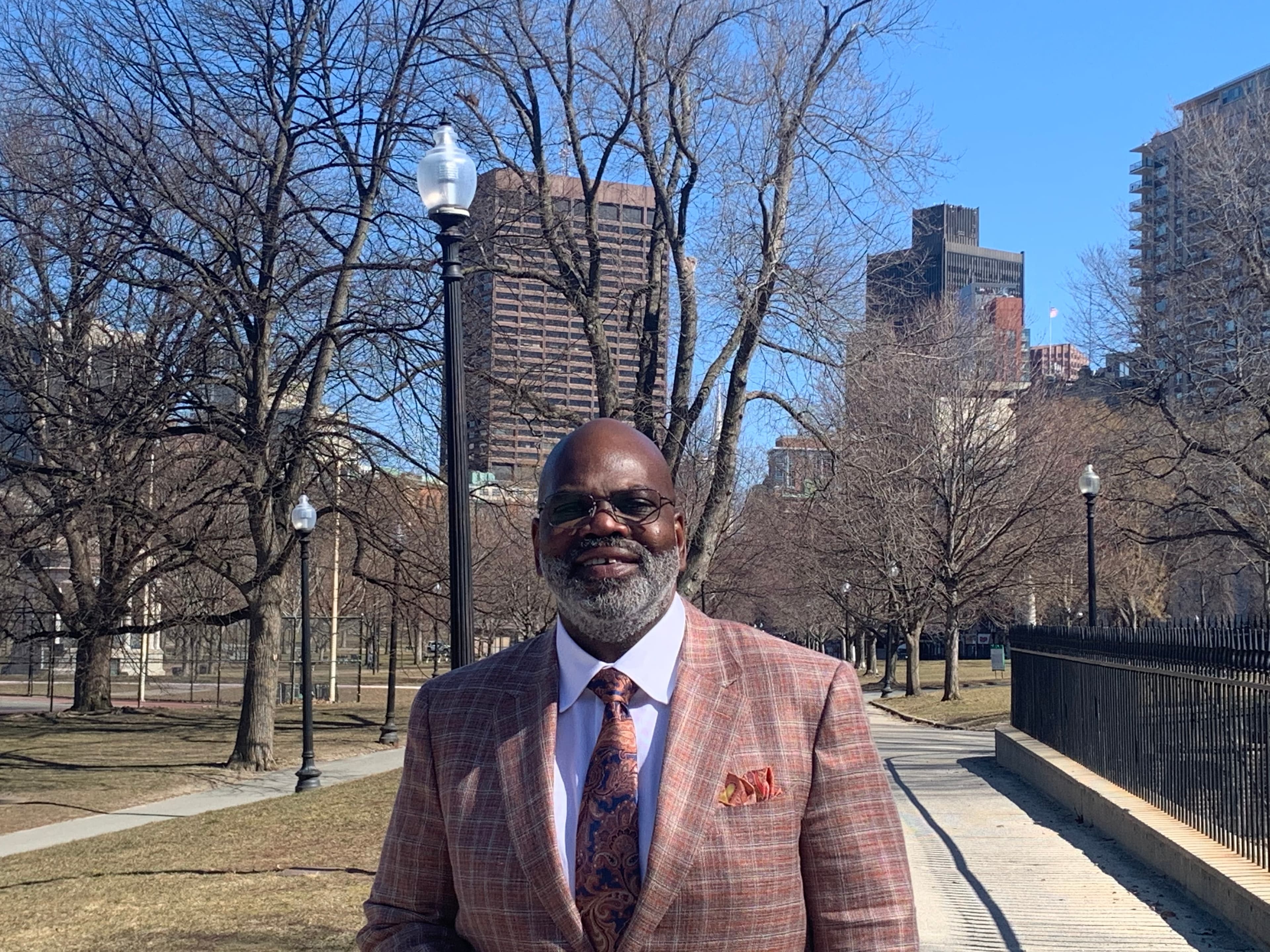 Smiling Black man with a beard in a patterned blazer and tie in a park.